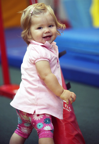 A little girl in a pink shirt standing in a gym.