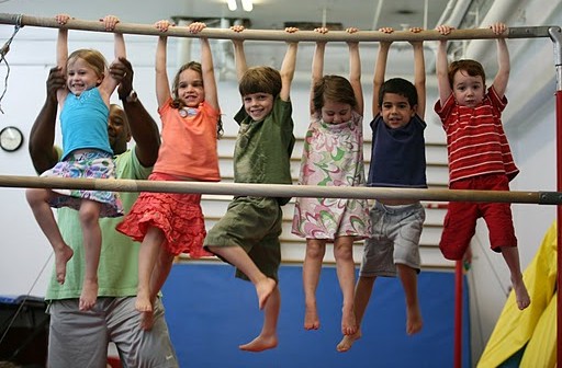 A group of children hanging on a bar in a gym.