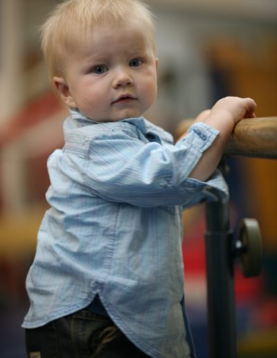 A young boy leaning on a bar in a gym.