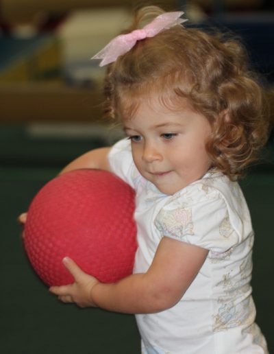 A little girl holding a red ball.