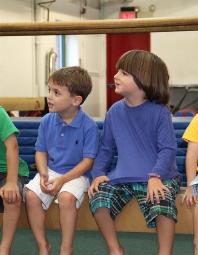 A group of children sitting on a bench in a gymnastics class.