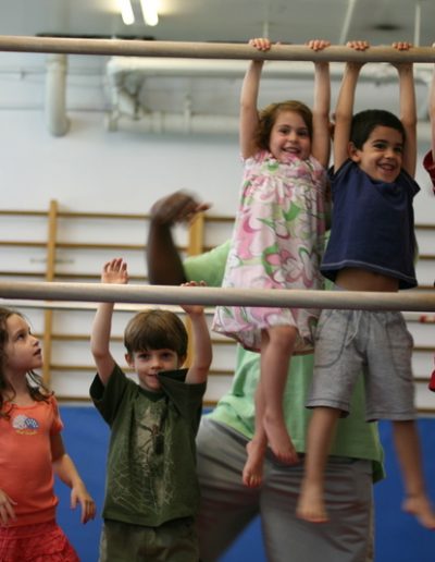A group of children are hanging on a bar in a gymnastics class.