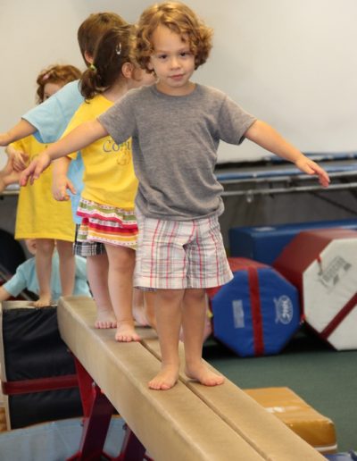A group of young children participating in gymnastics for kids on a balance beam at a toddler gym.