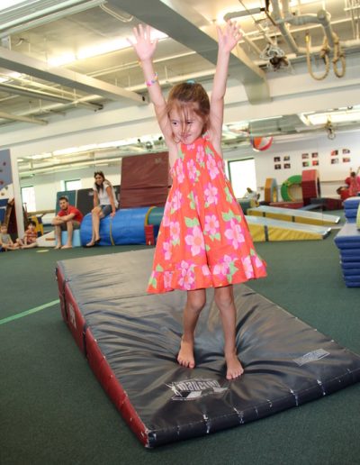 A little girl in a pink dress confidently balancing on a mat, showcasing her impressive gymnastics skills.
