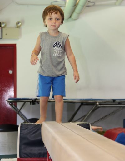 A young boy practicing gymnastics on a balance beam in a gym.