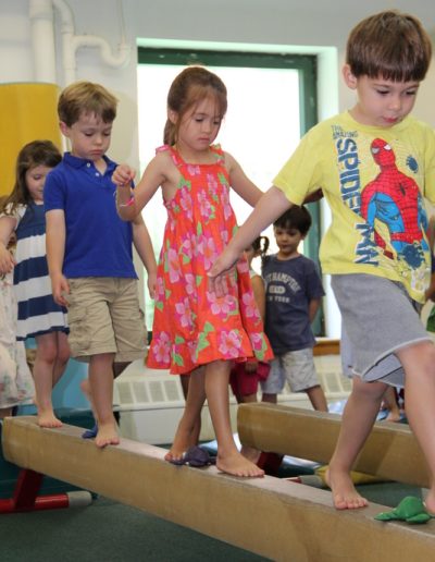 A group of children are playing on a balance beam during a gymnastics for kids class.