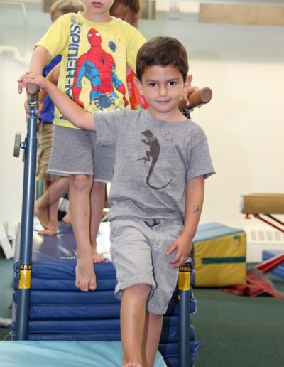 Two young boys standing on an exercise mat in a gymnasium during a gymnastics class for kids.