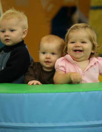 Three young children participating in gymnastics for kids, sitting on the floor in a gym.