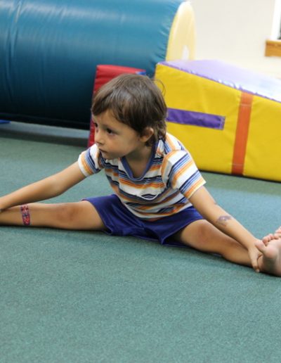 Two young children participating in gymnastics for kids, sitting on the floor in a gym.