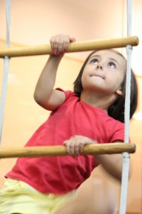 A young girl enjoying a birthday party at a toddler gym, confidently climbing a ladder as part of her gymnastics for kids class.