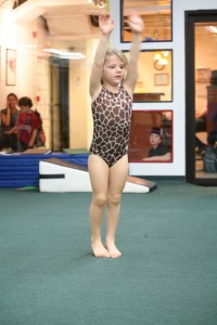 A little girl in a leopard print swimsuit showcasing her gymnastics skills, perfect for children's birthday parties.